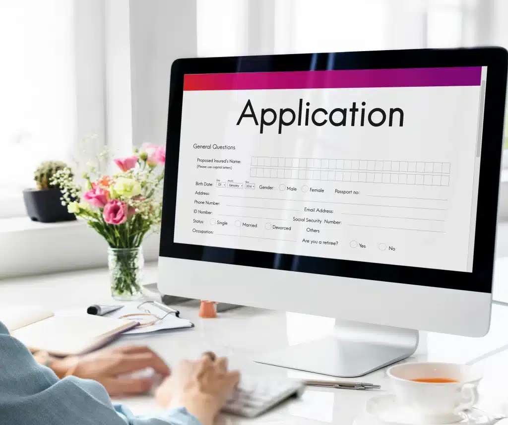 A computer screen showing application form beside a vase of flowers