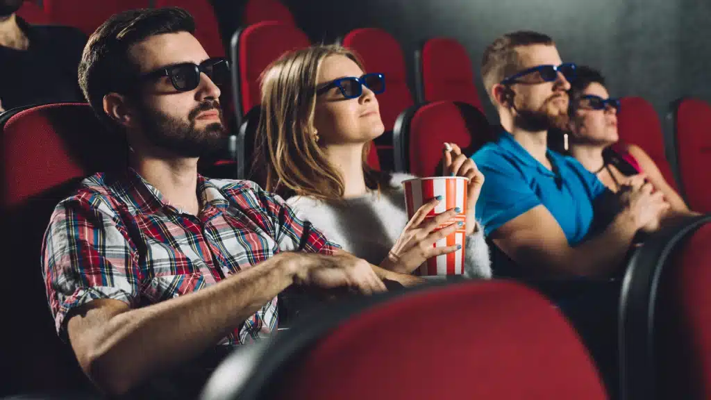 Two couples watching the movie and eating popcorns in the theatre.