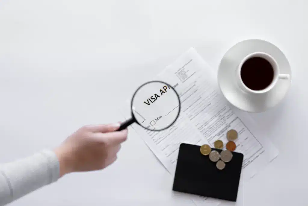 a person is magnifying visa application documents with the cup of coffee in white background